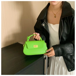 Detail of neon green handbag with knot handle and gold twist lock on model