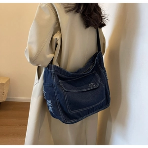 Dettaglio della borsa a tracolla in denim blu con cuciture bianche e nappe laterali