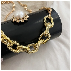 Detail of black acrylic cylinder bag with gold chain and large pearl floral ornament