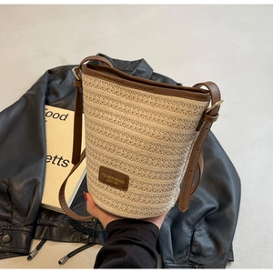Detailed macro of the woven straw bucket bag with brown leather trim and metal buckle detail