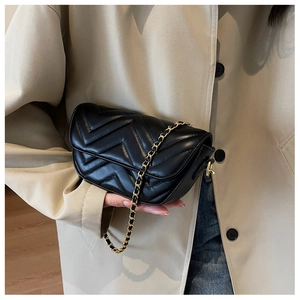 Detail of black V-quilted faux leather bag with elegant gold chain strap on a model