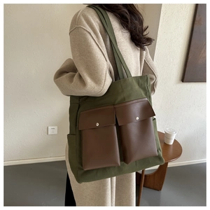 Rear view of a dark green canvas tote bag with brown leather front pockets worn by a model