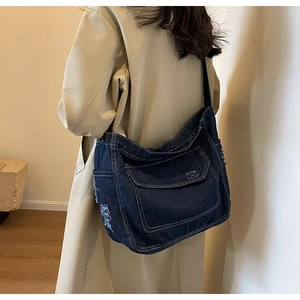 Dettaglio della grande borsa a tracolla in denim blu scuro con bordi sfrangiati su modella