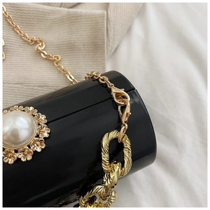 Detailed close-up of a black acrylic cylinder bag with a large pearl and golden flowers