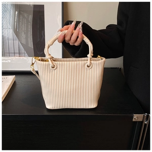Close-up of cream pleated bucket bag featuring round handle and gold hardware detail