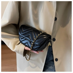 Detail of black chevron quilted leather bag with gold chain strap held by model