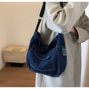 Dettaglio della borsa a tracolla in denim blu con bordi sfrangiati e tasca con fibbia