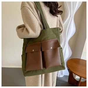 Detail view of olive green canvas tote bag with brown leather front pockets on model