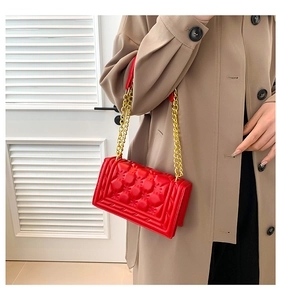 Detail of red quilted faux leather shoulder bag with gold chain strap on trench coat