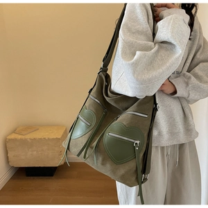 Detail shot of green canvas tote bag featuring large heart-shaped leather zipper pockets