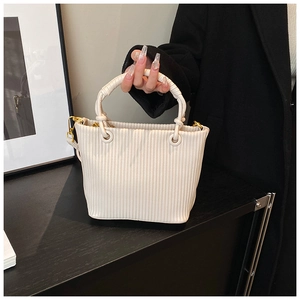 Close-up of cream pleated tote bag featuring knotted handle and gold metal hardware