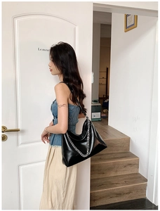Close-up of black patent leather tote bag with silver chain detail on a shoulder