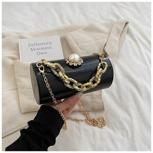 Detail of black acrylic cylinder bag with pearl ornament and gold chain strap