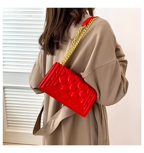 Detail view of the red crossbody bag featuring V-shaped stitching and gold chain strap