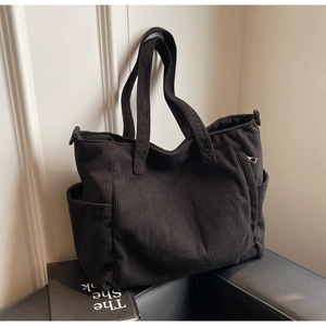 Detail view of black corduroy tote bag showing metal zipper pocket and textured side pockets