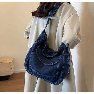 Dettaglio della borsa a tracolla in denim blu scuro con cuciture bianche e bordi a frange
