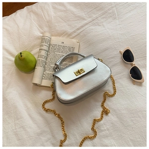 Detail of silver matte handbag with gold twist lock and metallic chain on white cloth