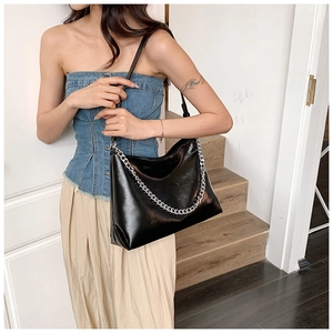 Detail of a black glossy leather tote bag with silver chain and leather shoulder strap