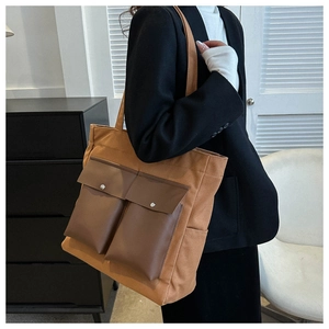 Close-up of brown canvas tote bag with dual leather front pockets and metal snaps