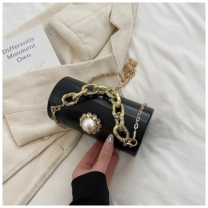 Detail of black acrylic cylinder bag featuring large pearl and golden chain strap