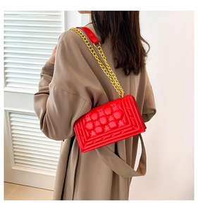 Detail of red pineapple embossed leather handbag with gold chain strap worn by a model