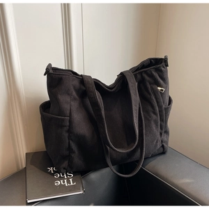 Close-up of black corduroy tote bag showing side pocket texture and metal D-ring detail