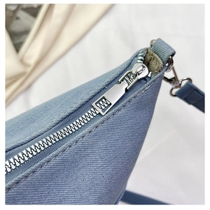 Detail of light blue canvas bucket bag showing silver zipper and metallic D-ring buckle