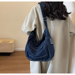 Dettaglio della grande borsa a tracolla in denim con cuciture a contrasto e bordi sfrangiati
