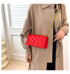 Detail of bright red geometric embossed leather handbag with golden chain strap on a model