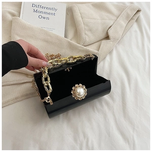 Detail of black acrylic clutch with pearl clasp, gold chain strap, and inner compartment