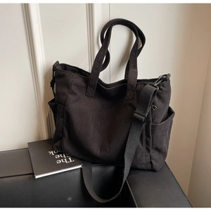 Detailed view of black corduroy tote bag featuring adjustable strap and side pocket