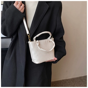 Detailed side view of a pleated cream bucket bag with knotted handle and gold hardware