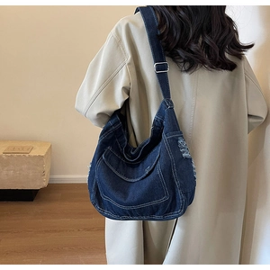 Dettaglio della borsa a tracolla in denim blu con bordi sfrangiati e grande tasca sulla spalla