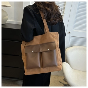 Detail of canvas tote bag showing dark brown leather flap pockets and metal buckles