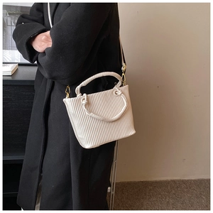 Vertical pleated cream white bucket bag shown on a black coat for high contrast view