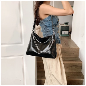 Detail of glossy black leather tote bag with thick silver chain handle on female model