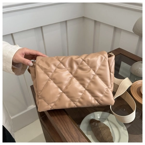 Dettaglio della borsa a tracolla beige trapuntata con texture morbida e ampia cinghia
