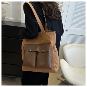 Detail view of brown canvas tote bag featuring premium leather utility front pockets