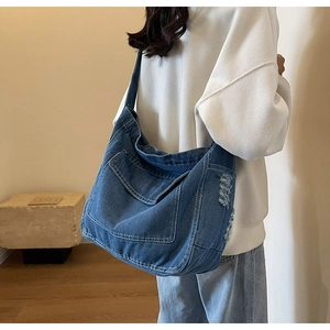 Dettaglio della borsa tote in denim blu con bordi sfilacciati e tasca sul modello