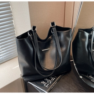 Detailed macro view of black lychee-textured leather tote with silver metal hardware accents