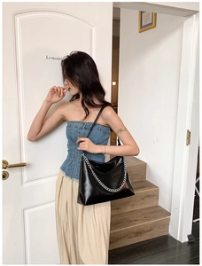 Detail of minimalist black faux leather tote with decorative silver chain and thin strap