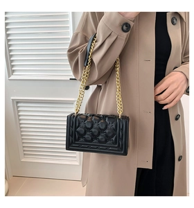 Detail of a black quilted shoulder bag with a gold chain strap and elegant flap closure