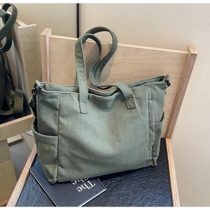Detailed close-up of light green corduroy tote bag texture and side pocket on wooden chair