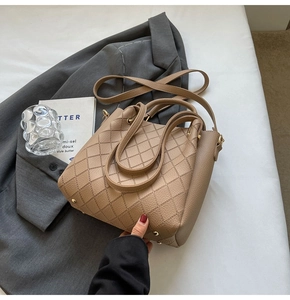 Detail of khaki leather bucket bag with quilted rhombic pattern on a grey suit background