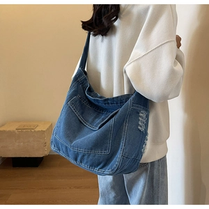 Dettaglio della borsa a tracolla in denim blu con cuciture bianche e trama usurata