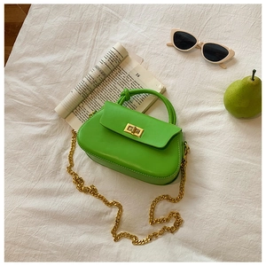 Flat lay of green leather handbag with gold chain strap and turn-lock closure on white fabric