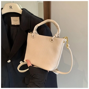 Detail shot of pleated cream bucket bag with golden metal hooks and braided handle