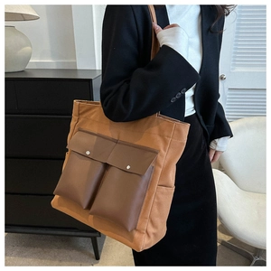 Detail of a large brown canvas tote bag with double front pockets on a model in a suit