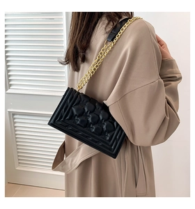Detail of black rectangular handbag with embossed texture and gold metal chain strap