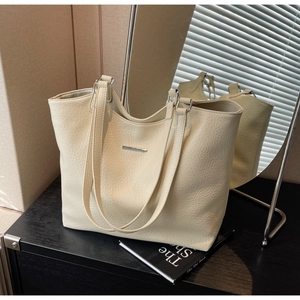 Detail of creamy white leather tote bag featuring a textured finish and metal trim accent
